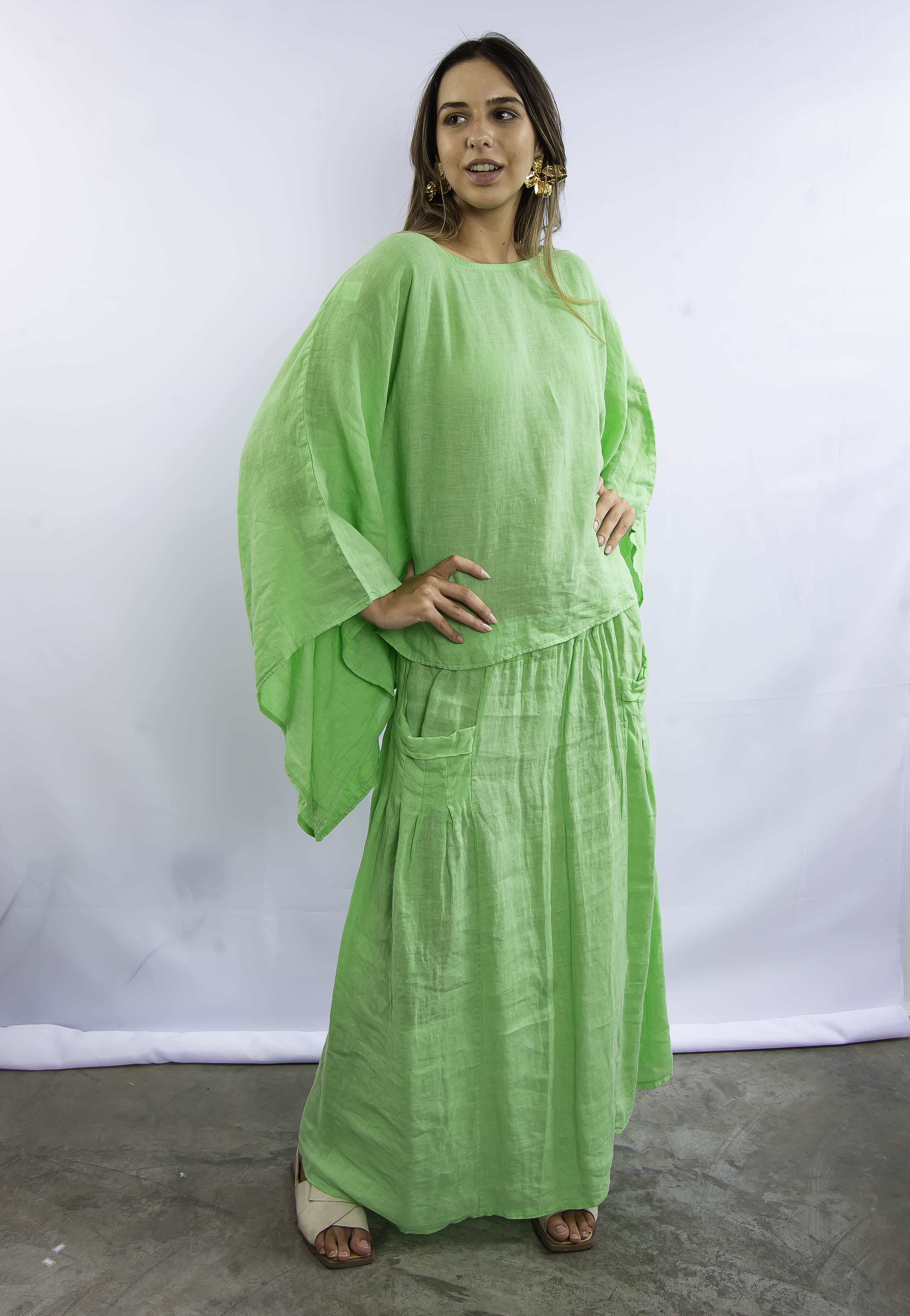 Modelo feminina em look verde vibrante, com blusa ampla e saia comprida em linho.