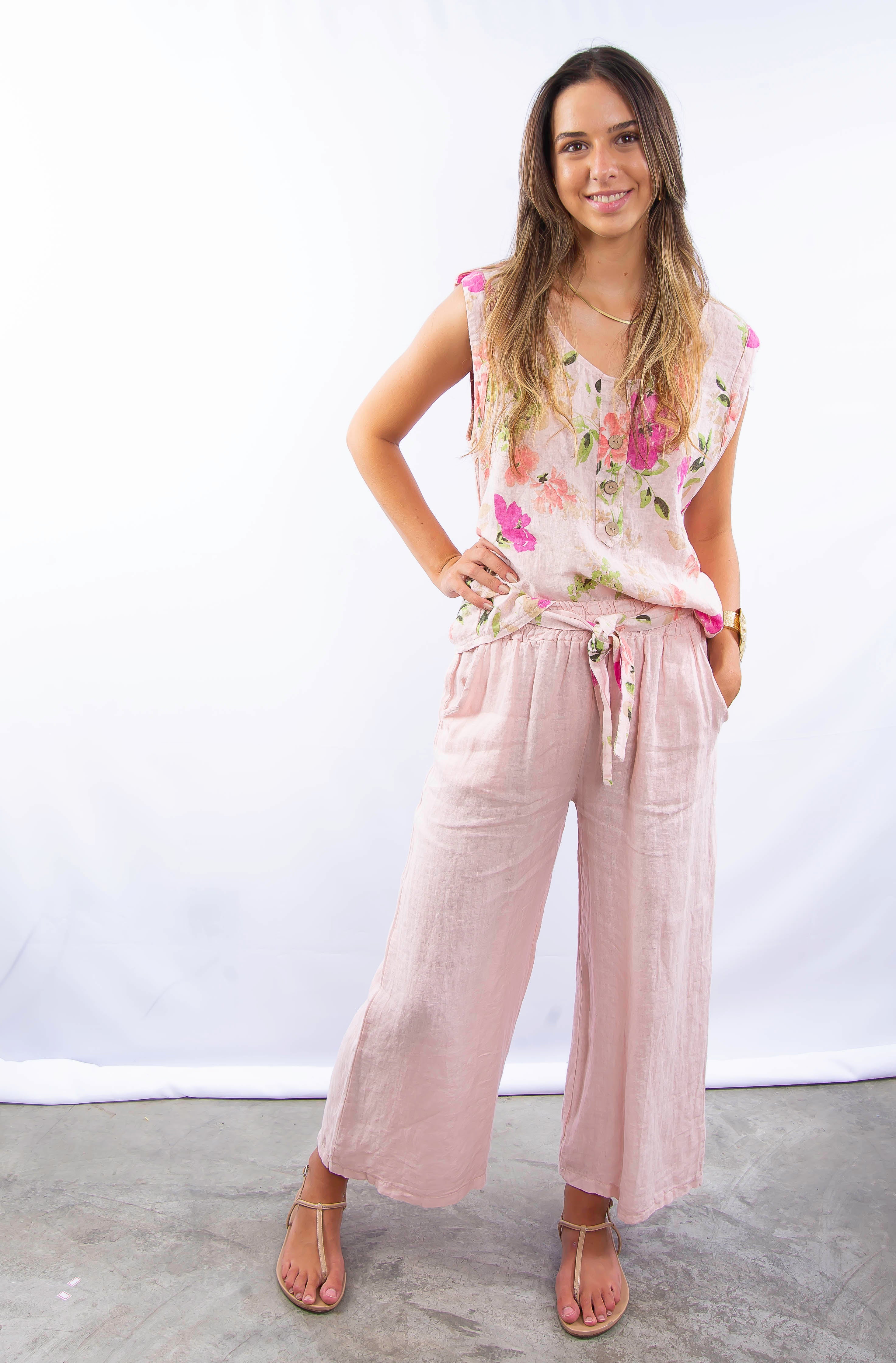 Mulher usando conjunto feminino com blusa floral sem mangas e calça de linho rosa.