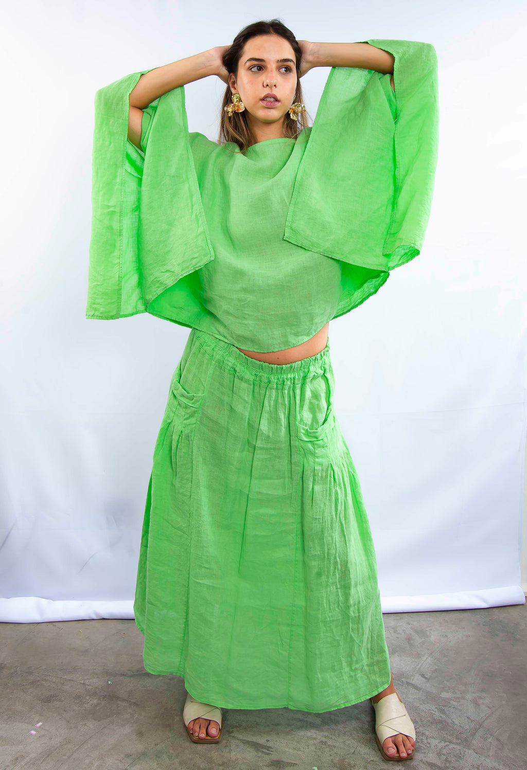 Mulher usando conjunto verde com blusa de mangas largas e saia longa, em pose frontal.