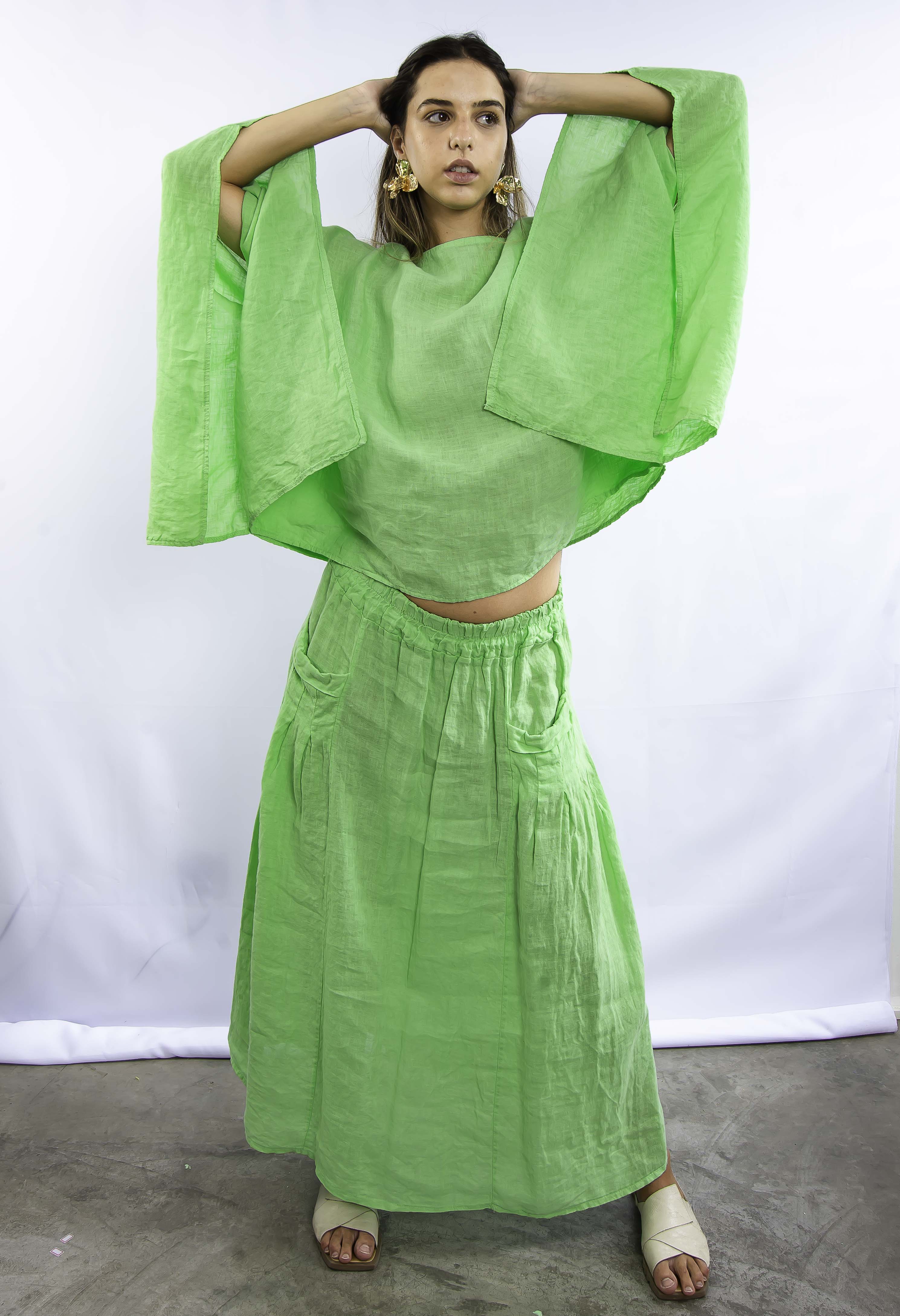 Mulher usando conjunto verde com blusa de mangas largas e saia longa, em pose frontal.