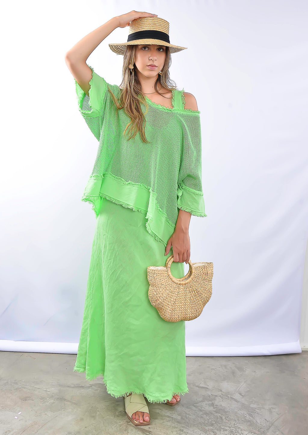 Modelo usando conjunto verde longo com blusa soltinha e saia, segurando bolsa de palha.
