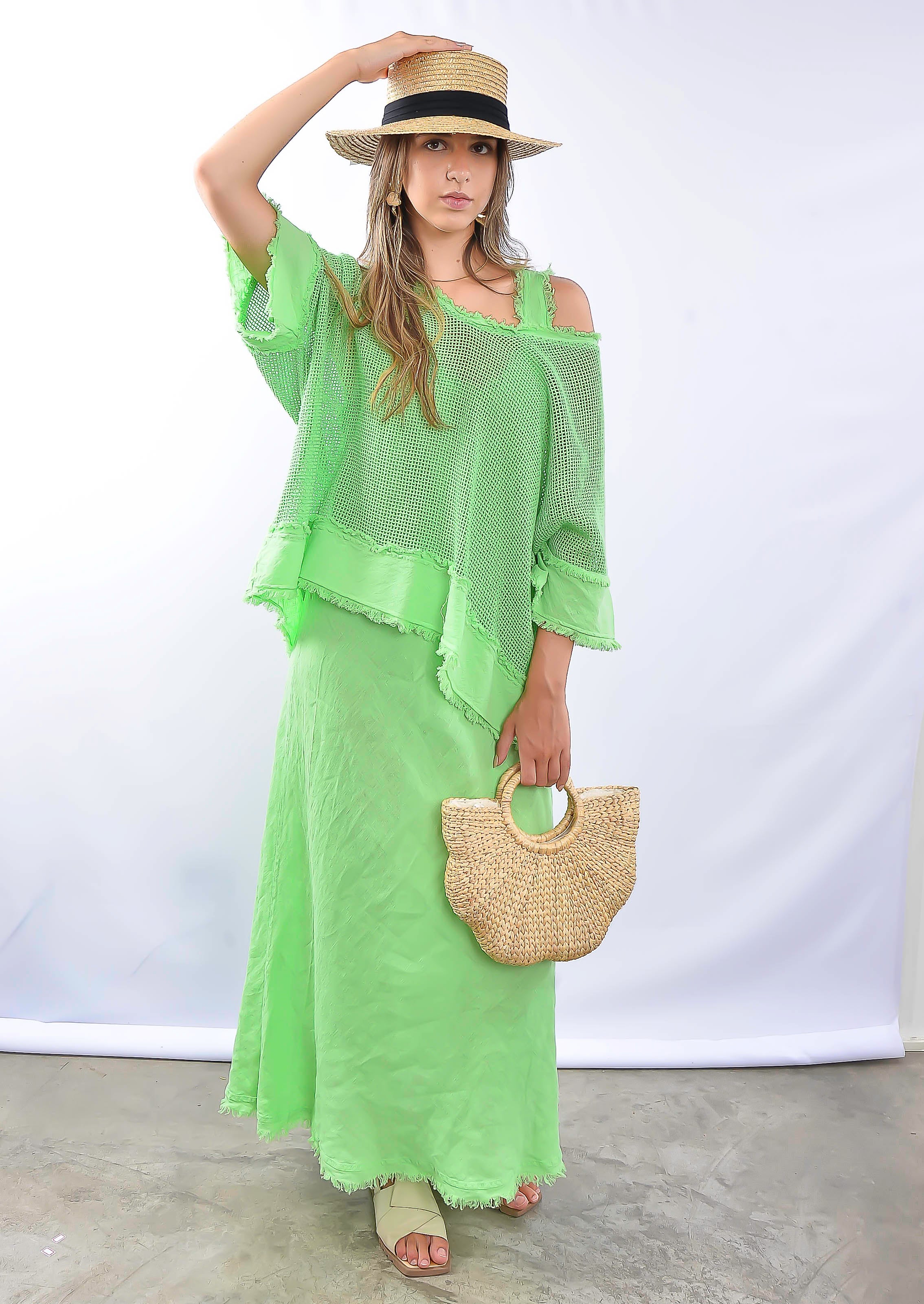 Modelo usando conjunto verde longo com blusa soltinha e saia, segurando bolsa de palha.