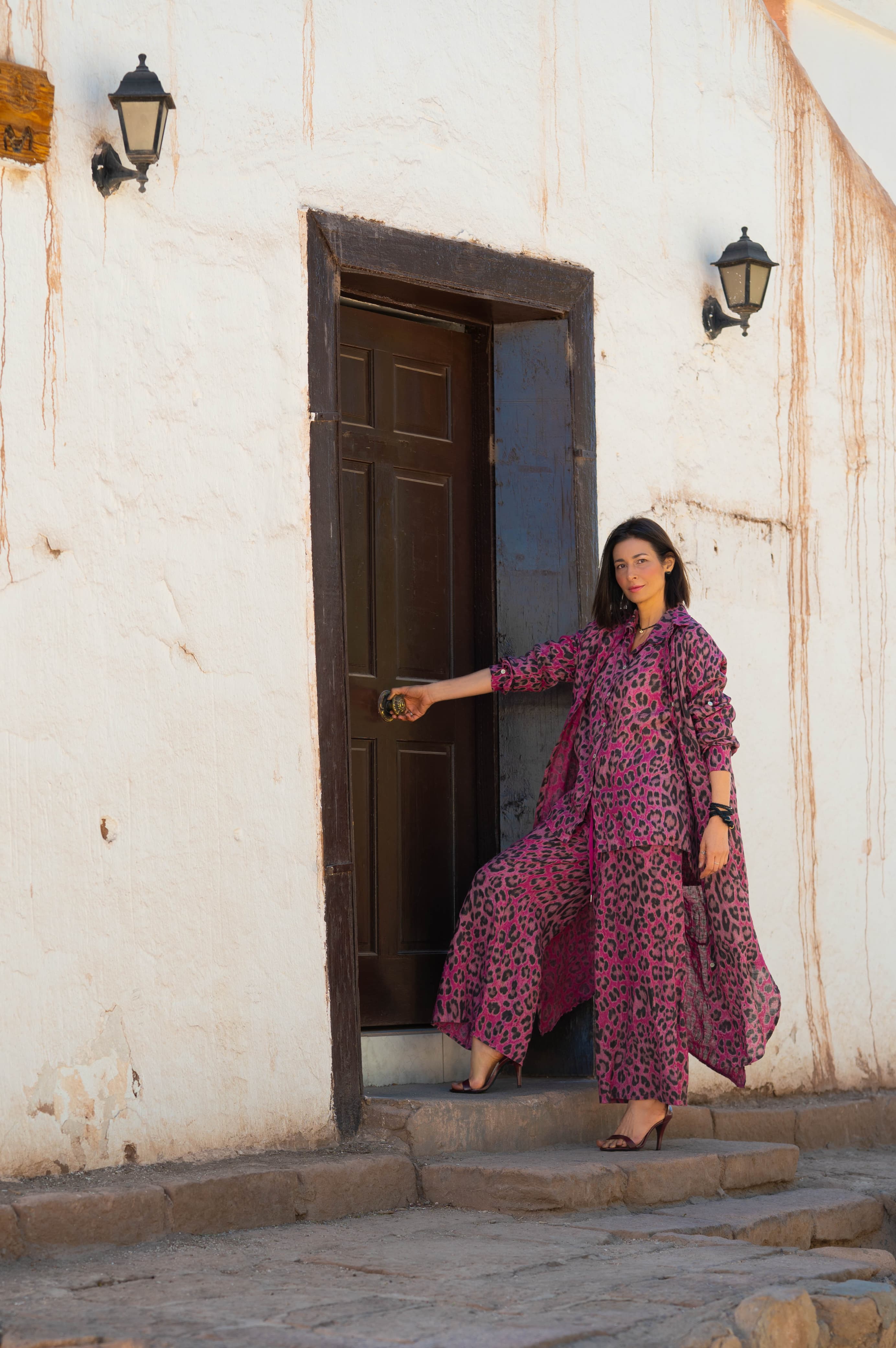 Mulher usando Vestido Piemonte longo em linho italiano roxo, em frente a uma porta rústica.
