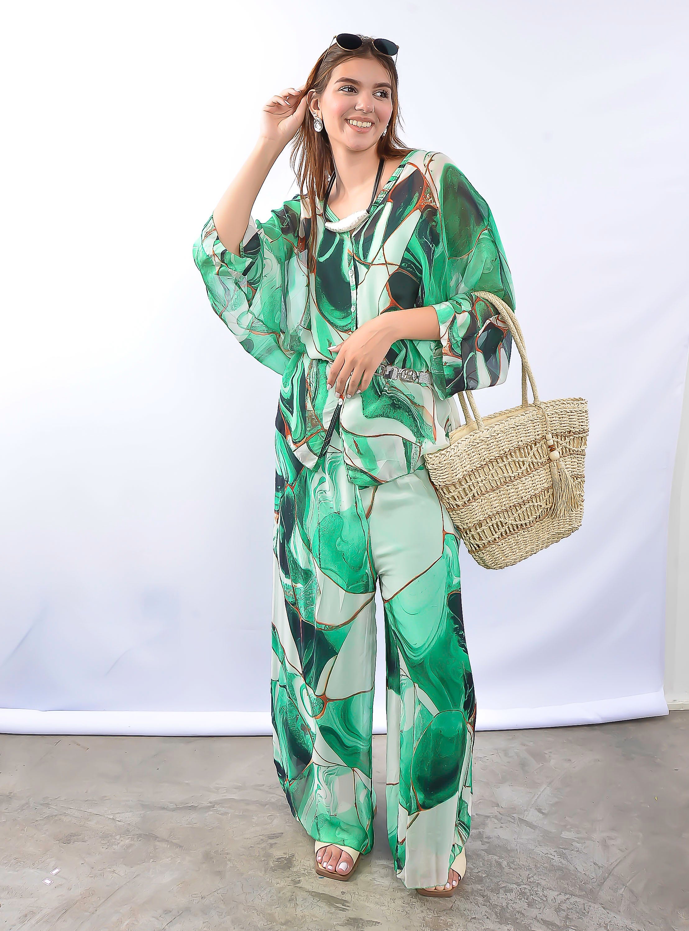 Modelo com vestido verde estampado segurando bolsa de palha.